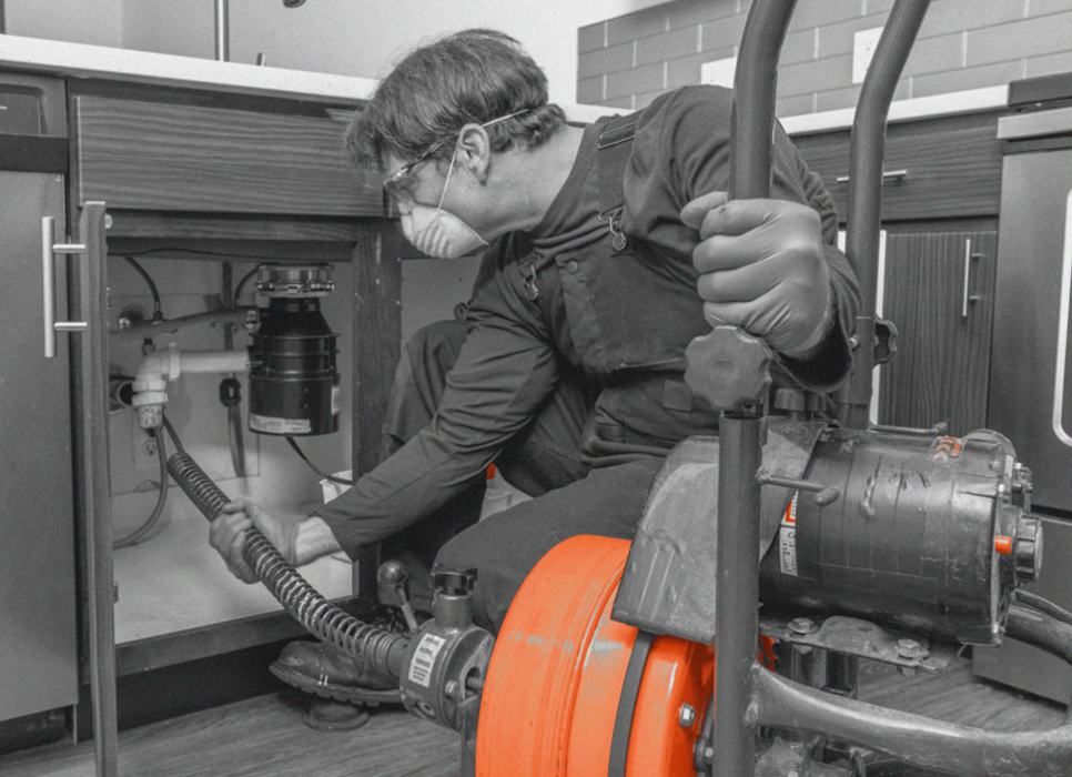 Technician clearing a drain line under a kitchen sink